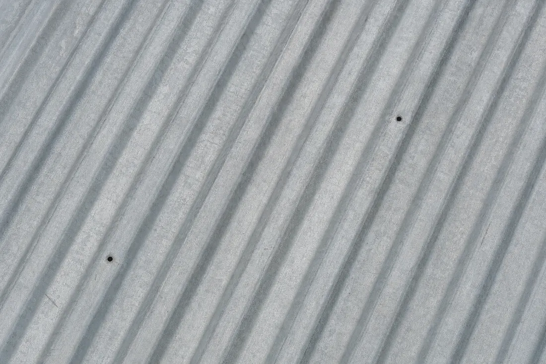 Tôle ondulée en aluzinc gris-argenté mat, patinée par le climat humide.